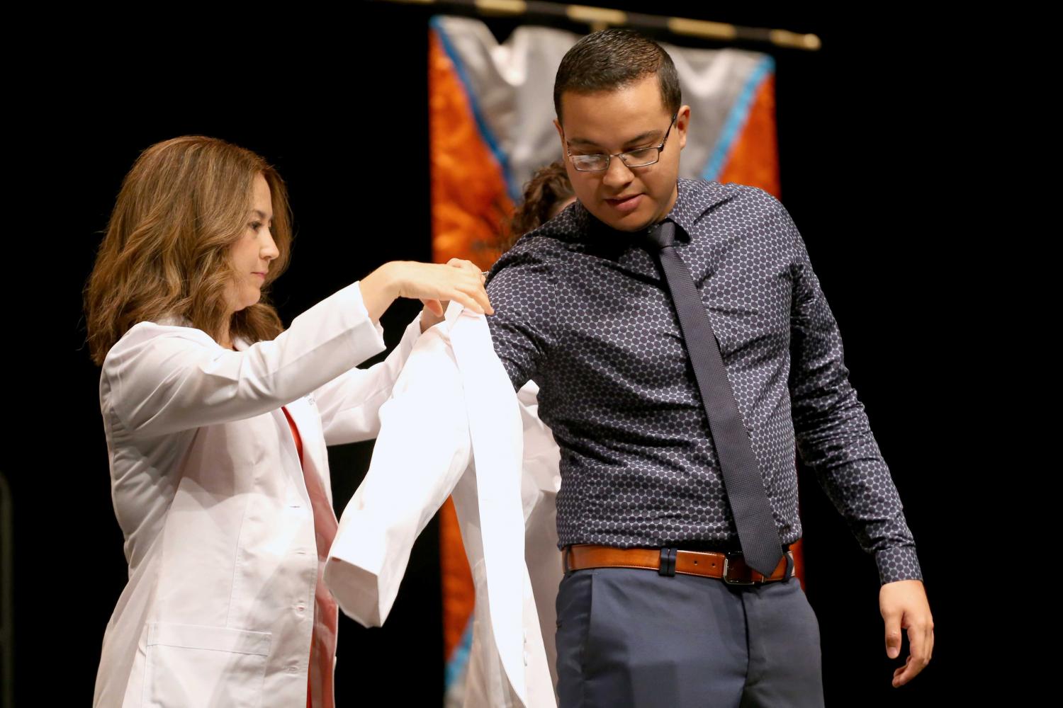 Director of experiential education clinical professor Jacquelyn P. Navarrete and chair of pharmacy practice and clinical sciences clinical professor Amanda M. Loya help students put on coats during the presentation of white coats.