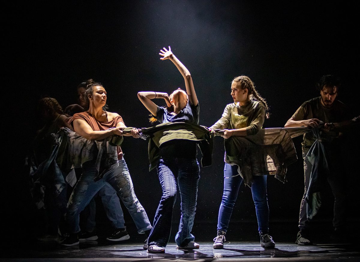 A performer reaches out as her fellow dancers hold her back in a scene from "Monomyth", illustrating the struggle between resistance and perseverance.